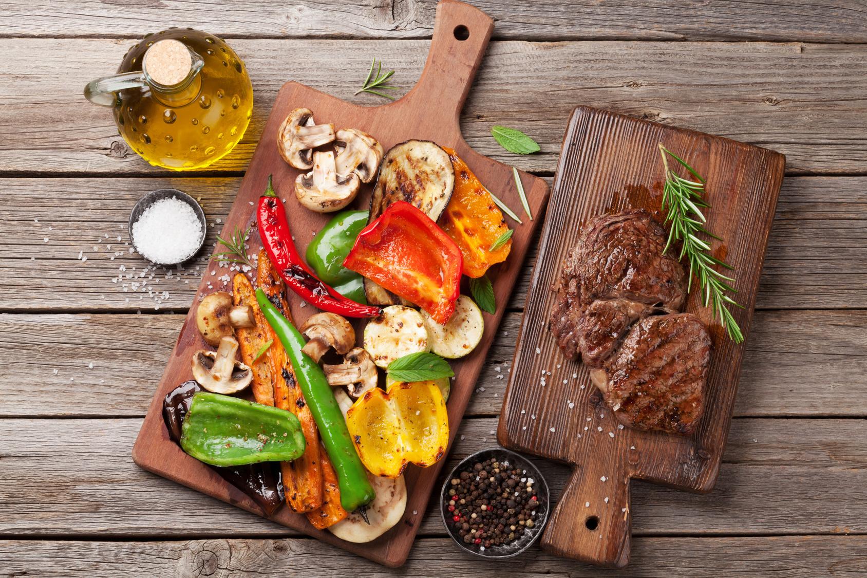 Grilled vegetables and beef steak on cutting board on wooden table. Top view