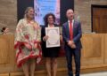 Cerimonia di apertura dell’anno accademico 2026-2027 della Nobile Accademia Leonina. Una donna mostra un attestato di riconoscimento, affiancata da una donna in abito elegante e da un uomo in completo blu con cravatta rossa.