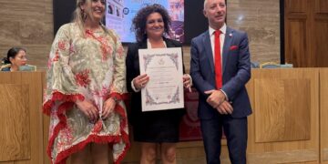 Cerimonia di apertura dell’anno accademico 2026-2027 della Nobile Accademia Leonina. Una donna mostra un attestato di riconoscimento, affiancata da una donna in abito elegante e da un uomo in completo blu con cravatta rossa.